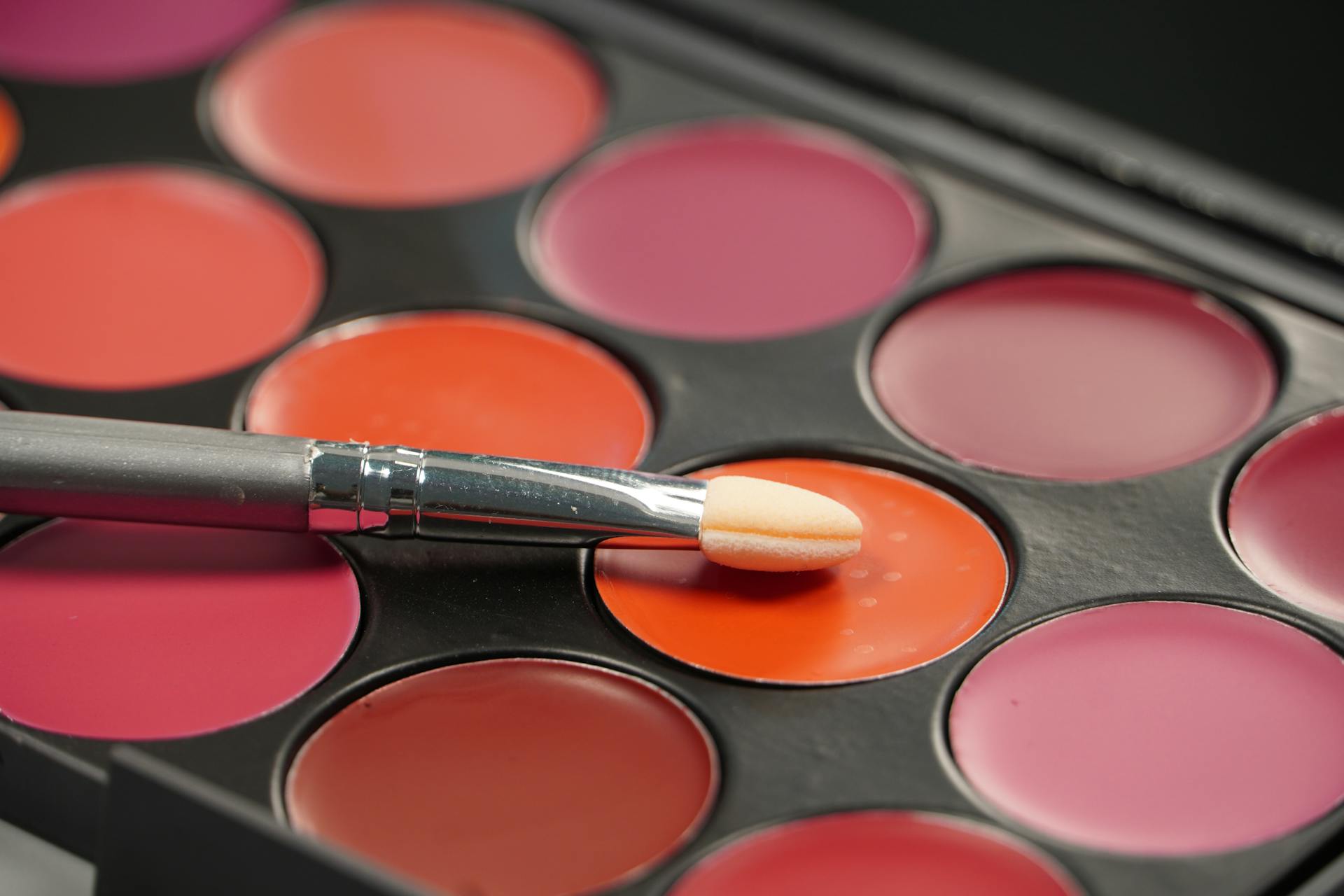 Close-up of colorful makeup palette with a brush resting on a vibrant red shade.