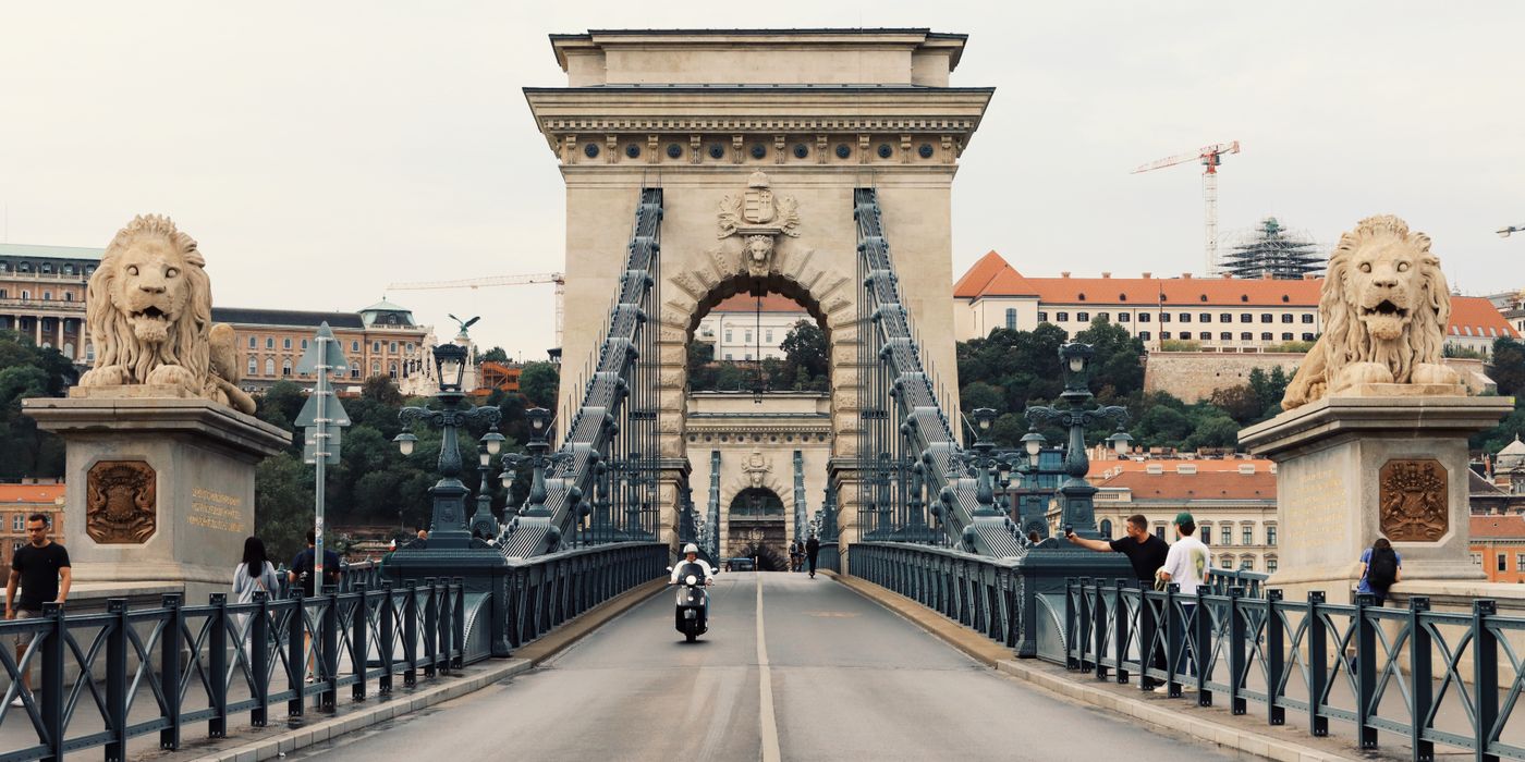 Iconic Széchenyi Chain Bridge in Budapest with tourists and lion sculptures on a clear day.