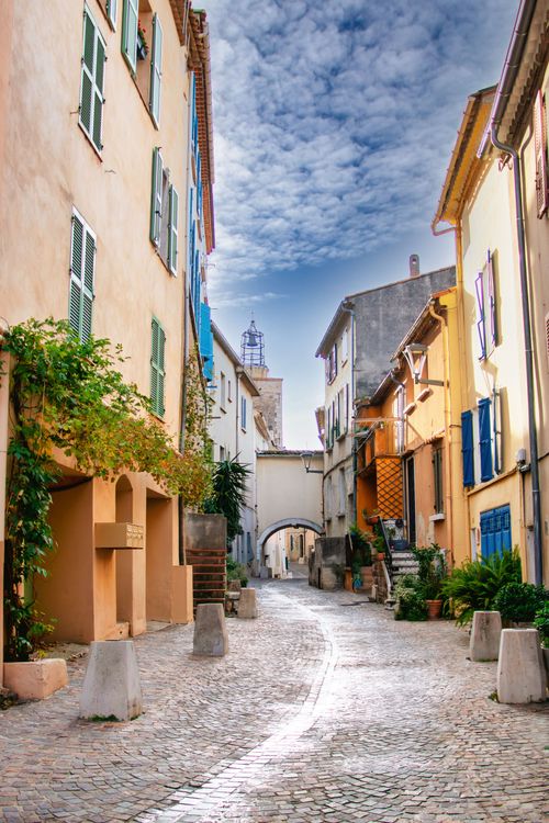 Free Beautiful empty narrow alley in a French town with colorful buildings and cobblestone pavement under a blue sky. Stock Photo