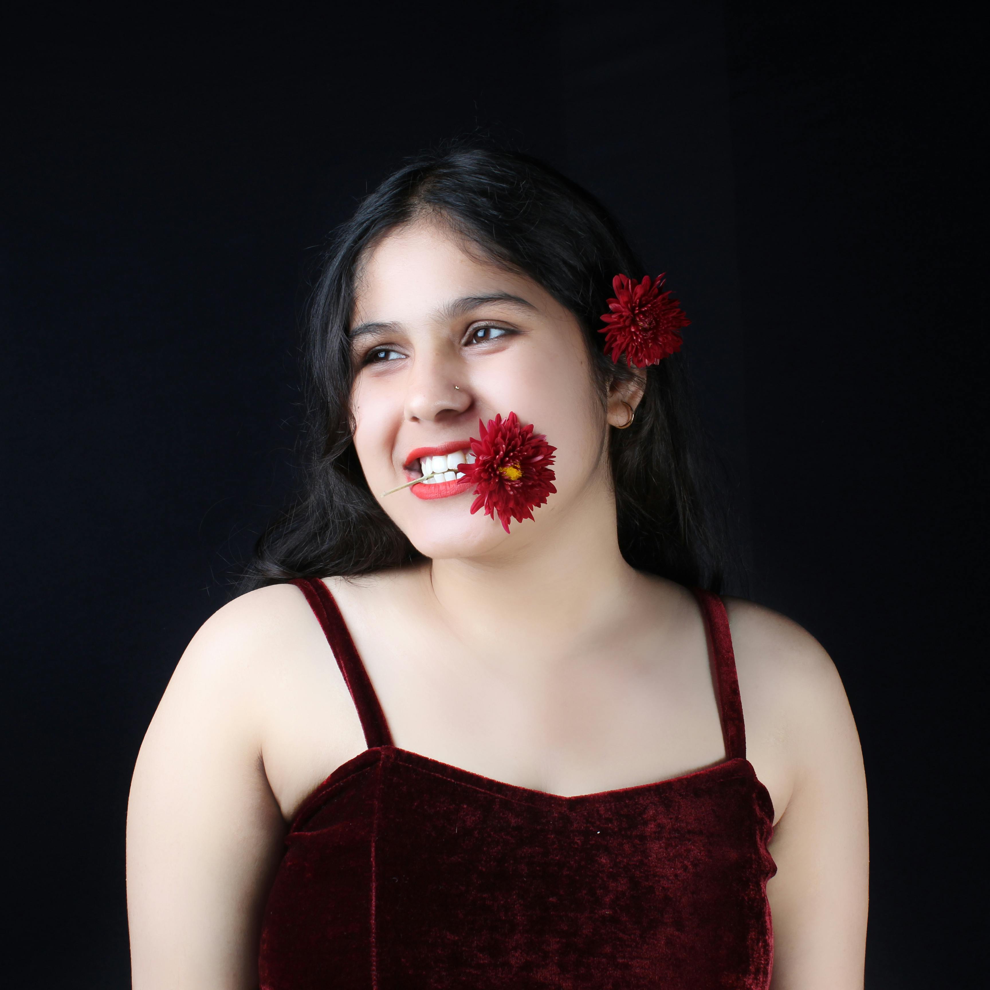 Portrait of a young Caucasian woman smiling with red flowers on black background.