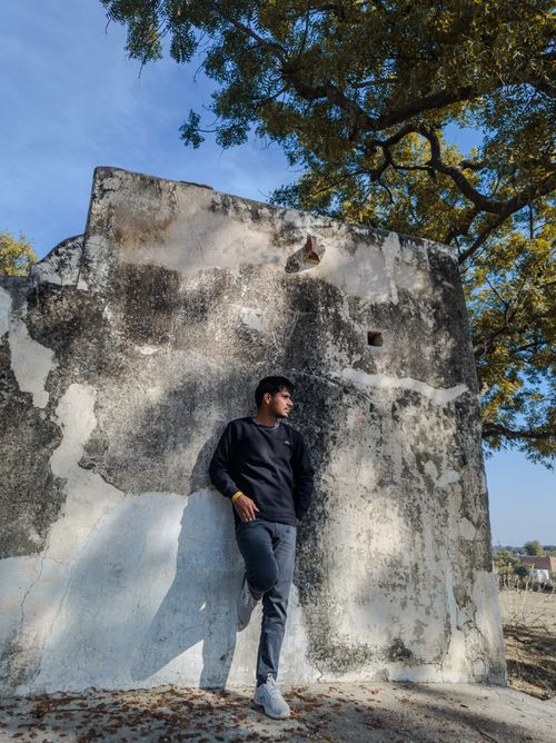 Free A man in casual attire leans against a weathered wall under a sunny sky, casting a shadow. Stock Photo