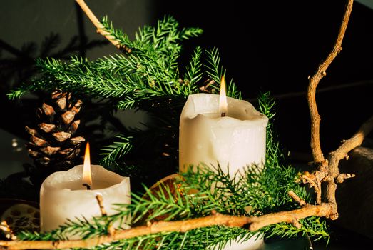 Close-up of burning candles surrounded by pine branches, cones, and twigs, creating a festive atmosphere.