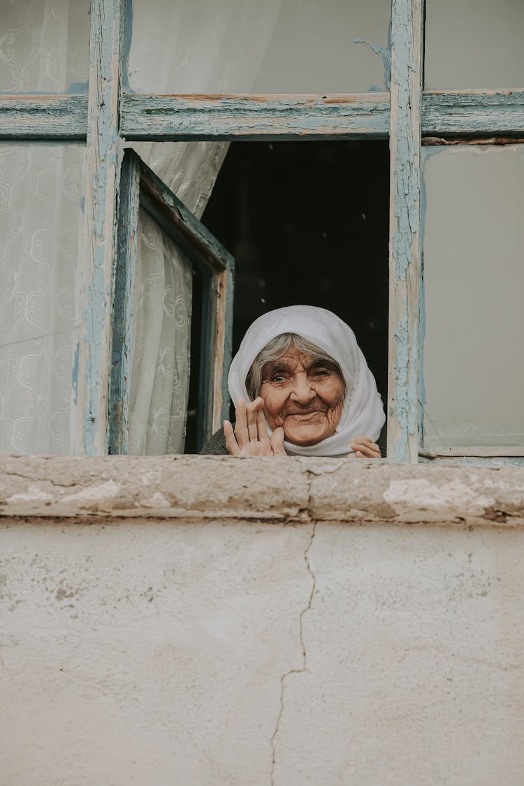 Elderly Woman Looking Out The Window And Waving