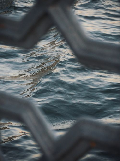 Free A unique perspective of ocean waves seen through a metal fence, creating an intriguing and abstract composition. Stock Photo