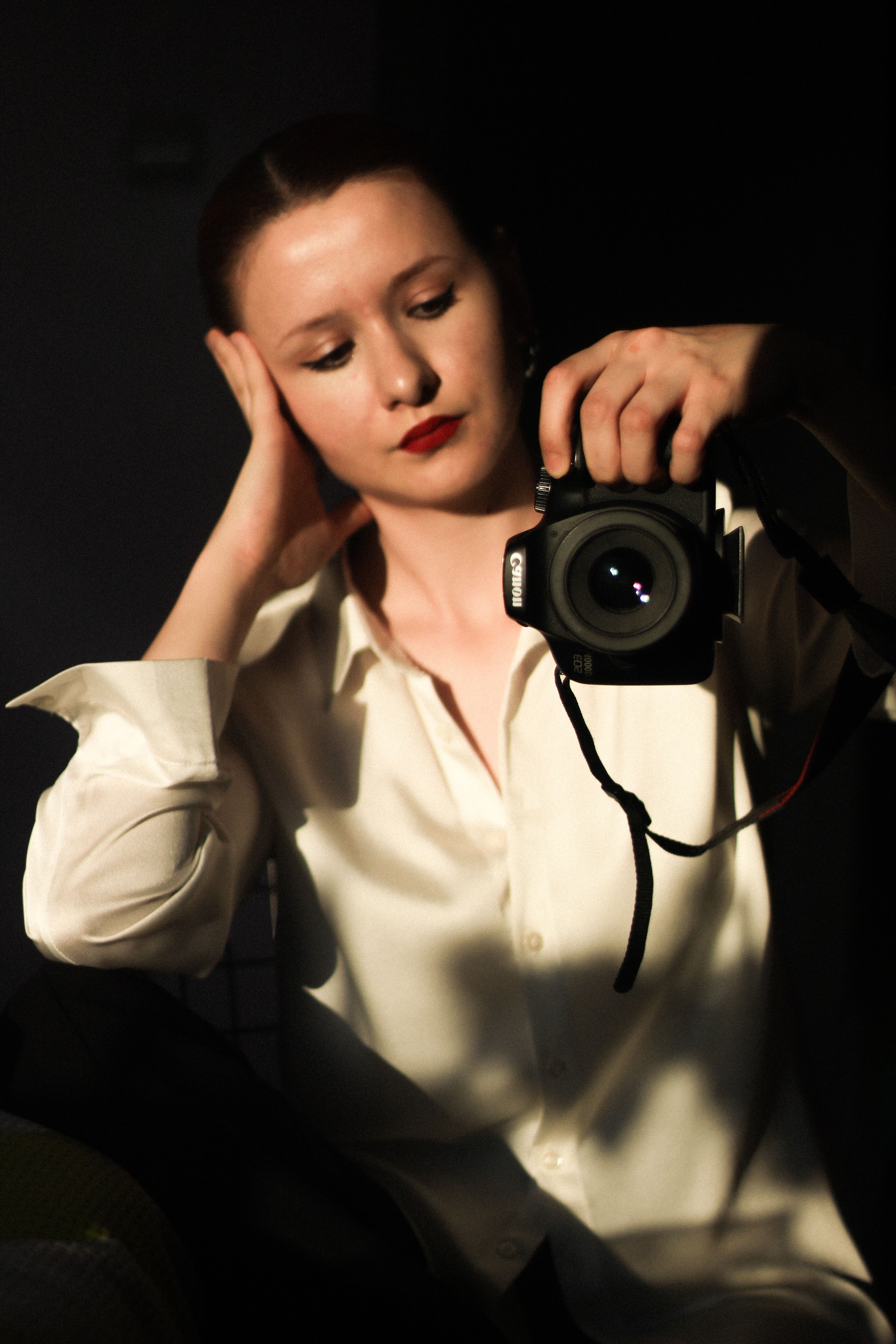 Portrait of a woman holding a DSLR camera and wearing a white shirt, captured in warm lighting.