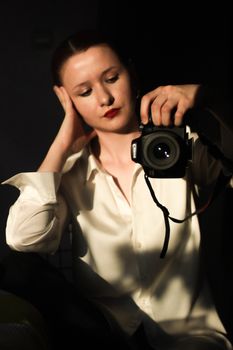 Portrait of a woman holding a DSLR camera and wearing a white shirt, captured in warm lighting.