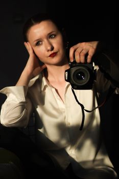 A woman holding a camera in a relaxed pose with soft lighting for a creative portrait.