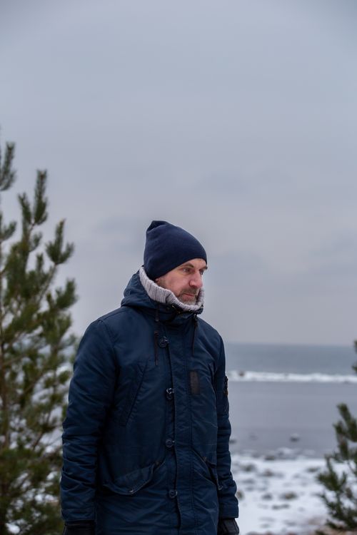 Free Man in winter coat and beanie standing by a snow-covered sea shore. Stock Photo