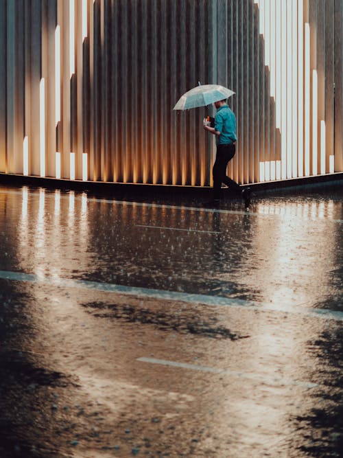雨が降っている間、建物の横を歩いている傘を持っている男の写真