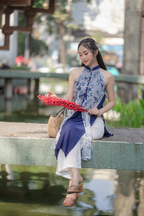 Young Brunette in Dress Posing with Flowers by River