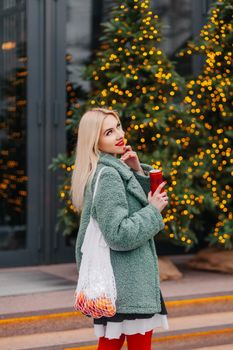 Stylish woman in Zermatt embraces winter fashion amidst Christmas lights, holding a festive drink.