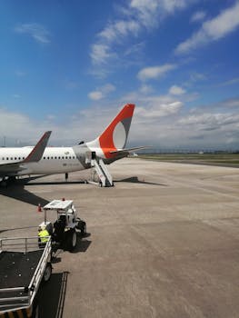 Airplane on airport tarmac with clear sky and luggage vehicle in the foreground.