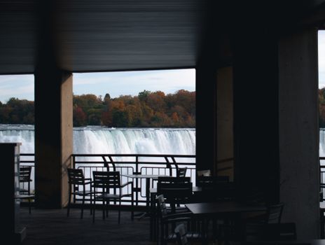A picturesque view of Niagara Falls framed by a balcony with autumn foliage in the background.