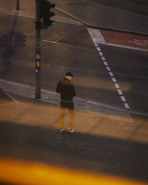 Free A man stands alone on a Berlin street corner during twilight, casting long shadows. Stock Photo