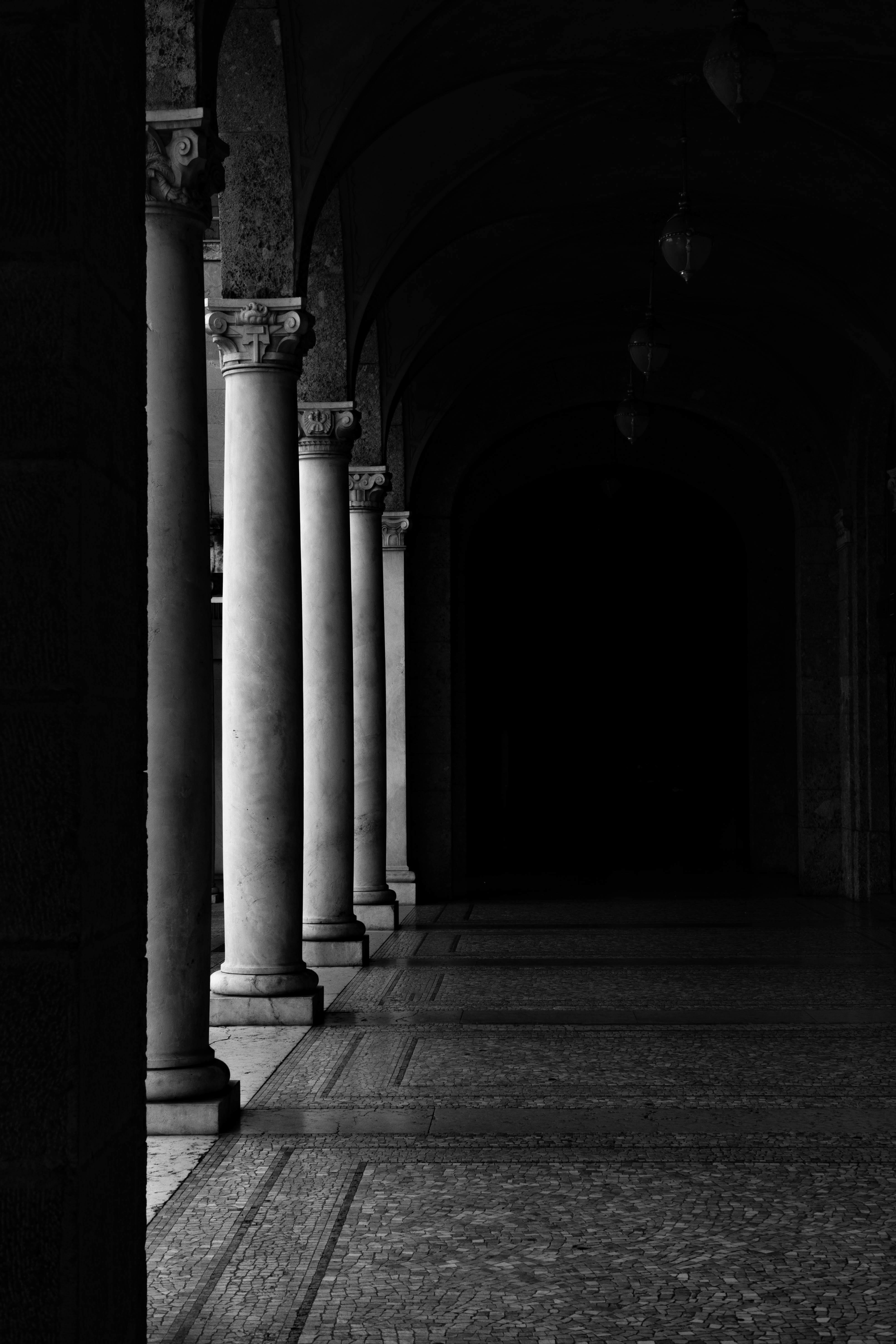A monochrome image showcasing classic columns in a shadowed corridor, creating a dramatic ambiance.