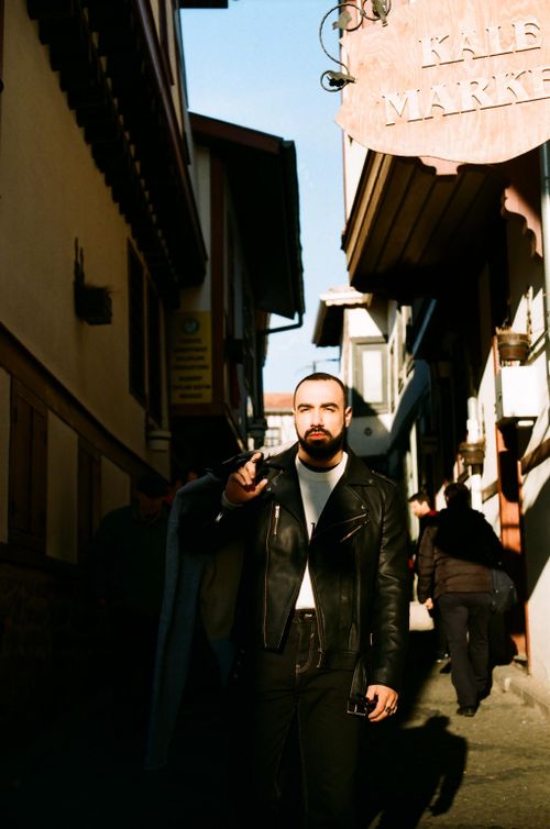 Free Man in leather jacket standing in a narrow, sunlit alley street scene. Stock Photo