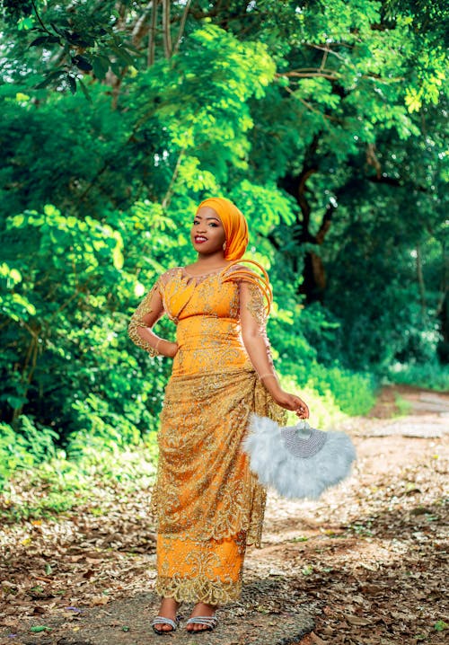 Smiling Woman in Traditional Clothing Standing on a Path Holding a Fan