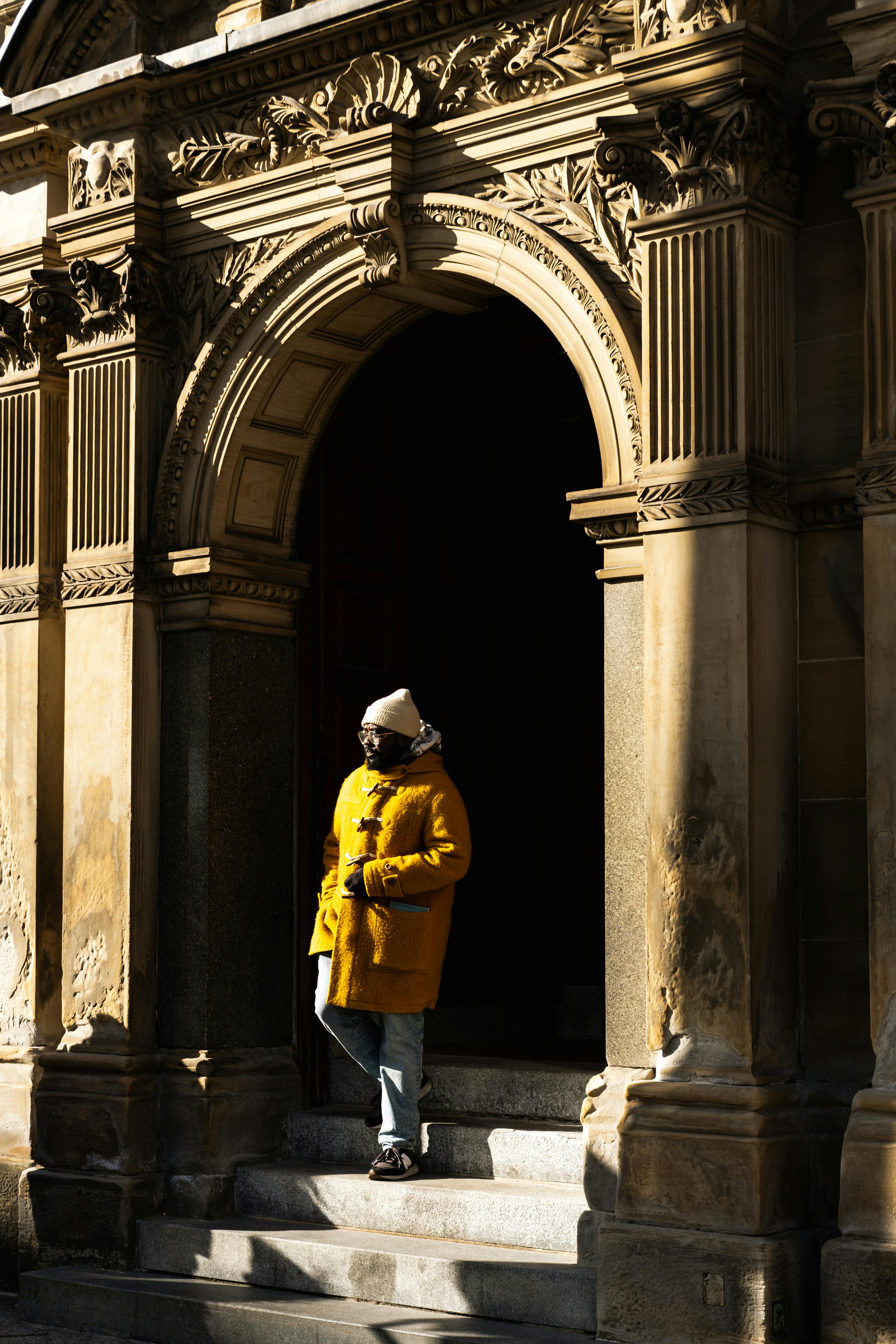A man in a yellow jacket stands under an ornate archway in Toronto, Canada.