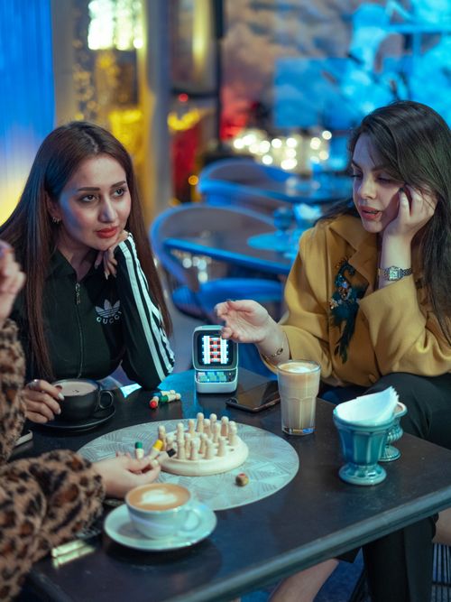 Free Women sipping coffee and chatting at a cozy café table with a game. Stock Photo