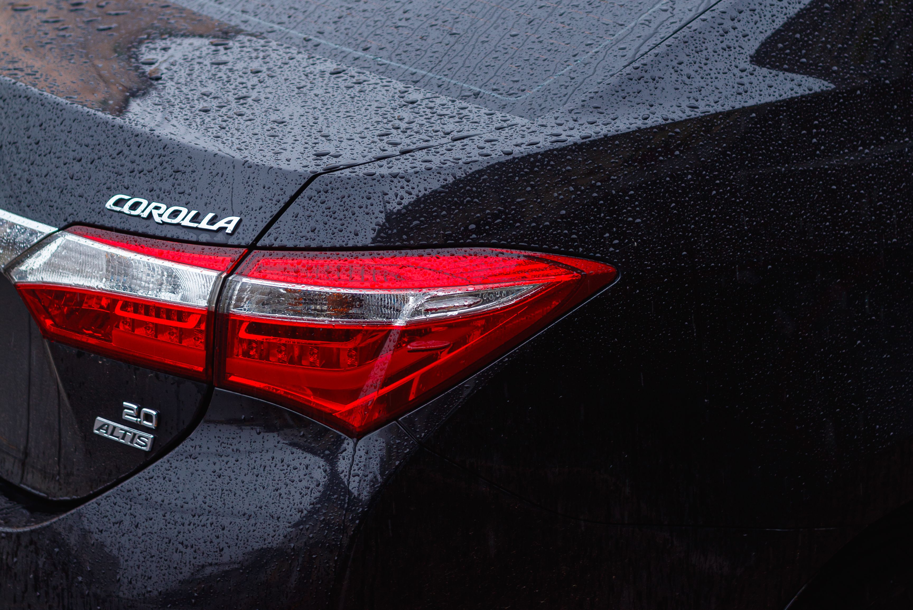 Free Detailed rear view of a Toyota Corolla in the rain, showcasing raindrops on the car surface. Stock Photo