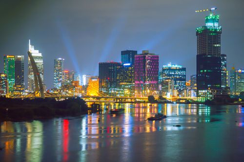Free A vibrant city skyline reflecting on a river with illuminated skyscrapers and a bridge at night. Stock Photo