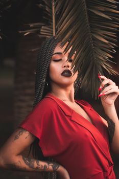 穿着红色连衣裙的时髦女人与热带树叶合影，散发着优雅与神秘
