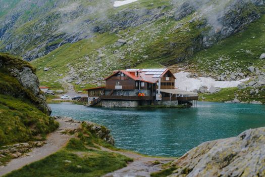 Serene mountain lodge by Balea Lake, surrounded by lush greenery and rocky hills.