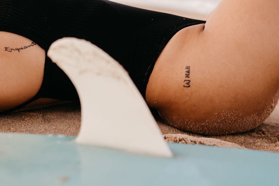 Woman lying on sandy beach with tattoos visible, enjoying a summer day.