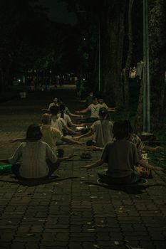 Group of people meditating outdoors at night on a paved path in an urban park setting.