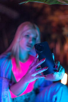 Blonde woman capturing a selfie on her smartphone with vibrant lighting.