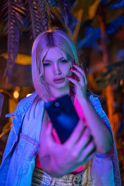 Blonde woman taking a selfie with a smartphone under vibrant neon lights at night.
