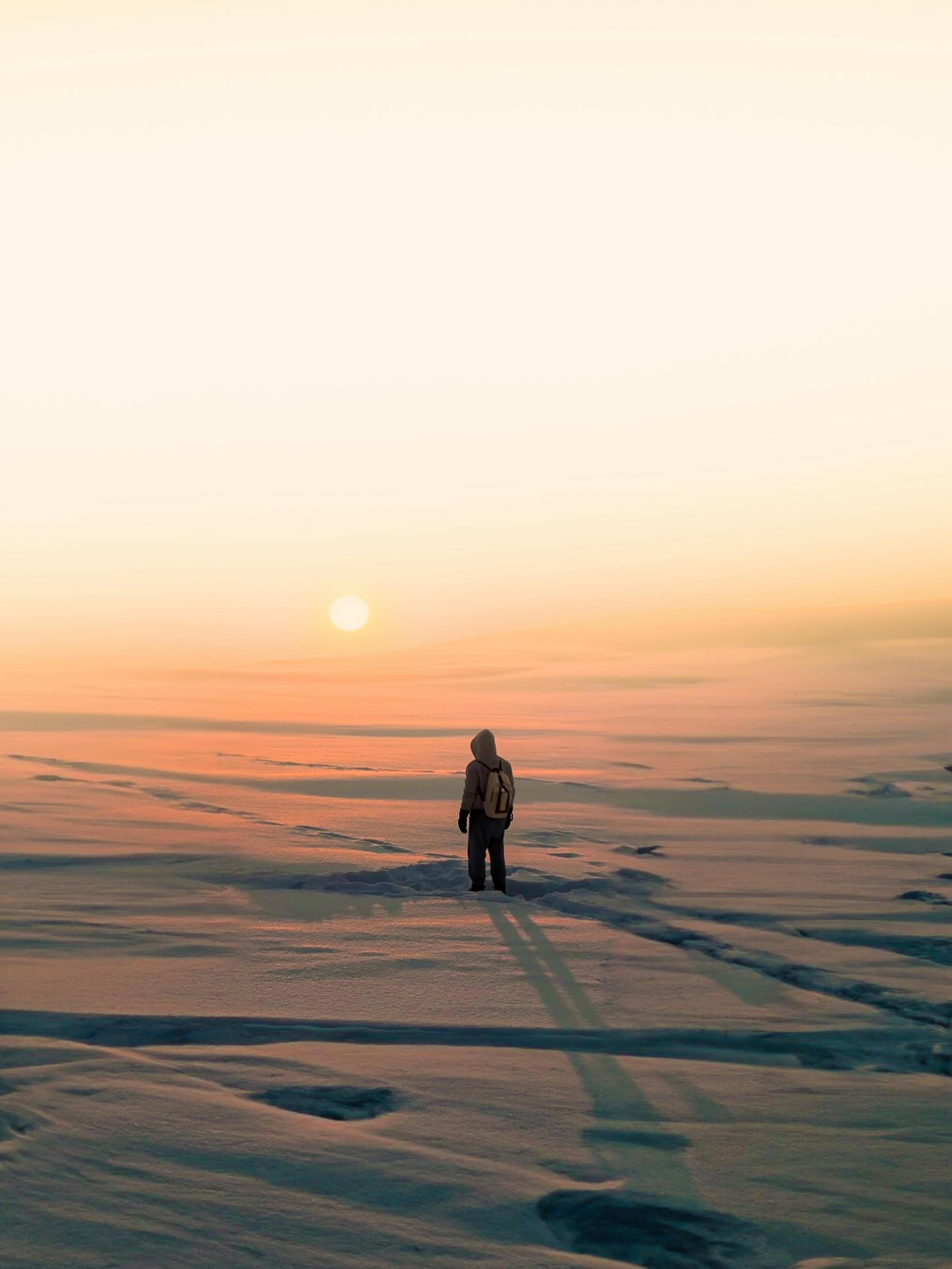 A lone hiker stands on snowy plains at sunset, showcasing winter solitude and adventure.