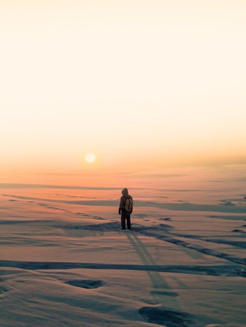A lone hiker stands on snowy plains at sunset, showcasing winter solitude and adventure.