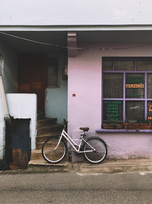 Free A white bicycle rests against a pastel pink house in a quaint urban street scene. Stock Photo