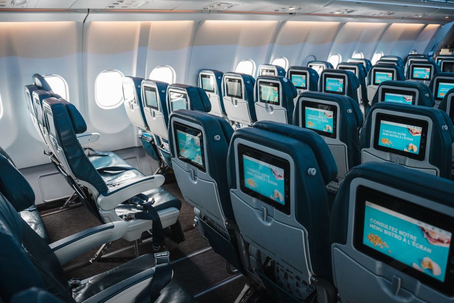 Rows of empty economy seats with seatback screens in an aircraft cabin