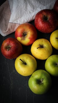 Vibrant red, green, and yellow apples arranged on a dark surface with white cloth background.