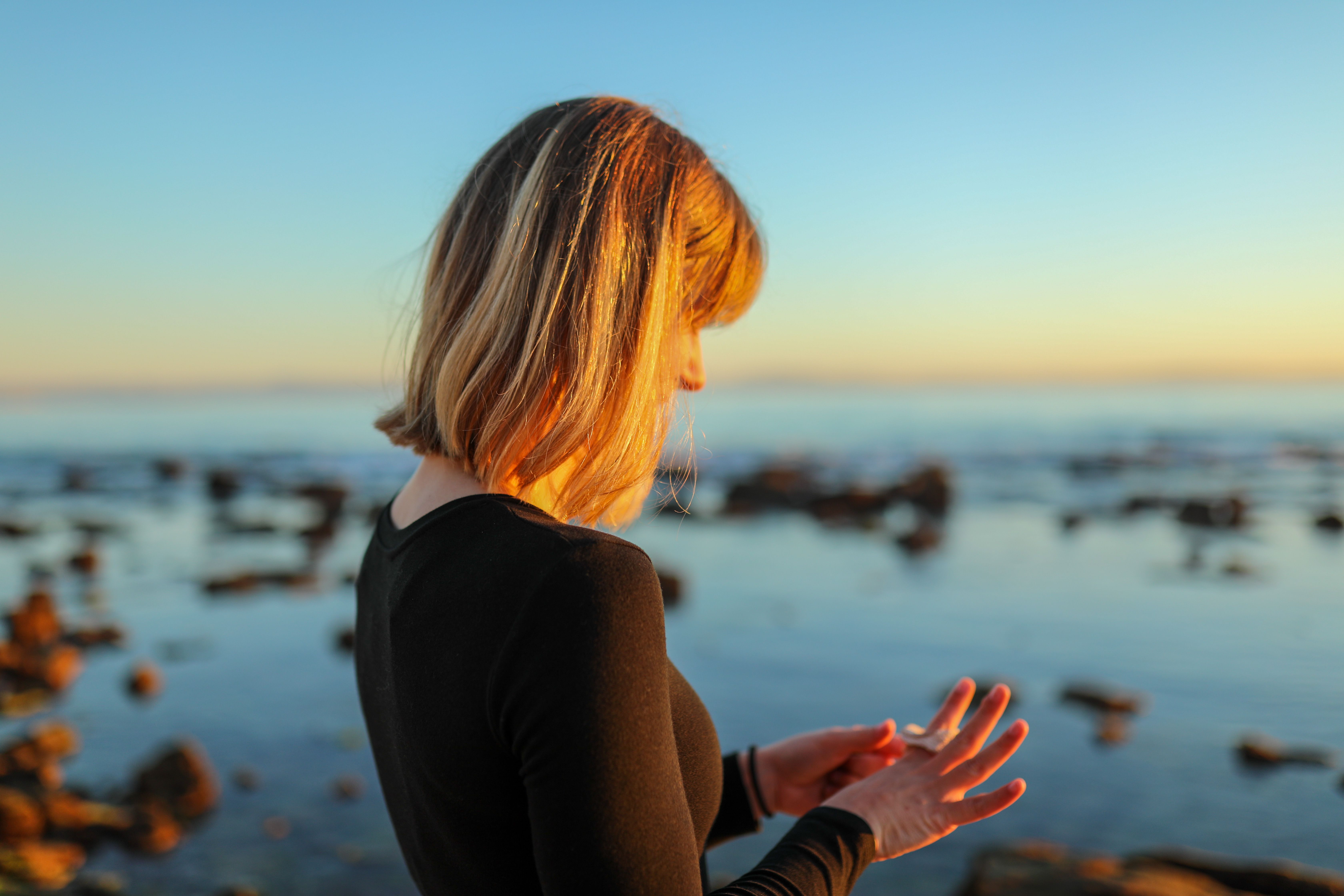A woman in a black blouse stands quietly at the Tarifa coast during sunset, contemplating the sea.
