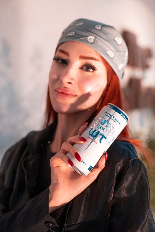 Free Portrait of a woman holding an energy drink can, wearing a headscarf in natural light. Stock Photo
