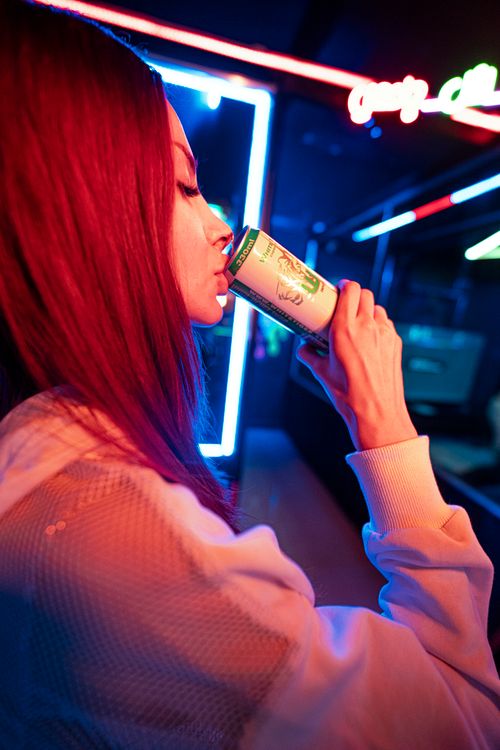 Free A woman sipping a beverage in a lively, neon-lit nightlife setting, conveying energy and style. Stock Photo