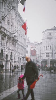 A bustling European city street on a rainy day with people and historic architecture.