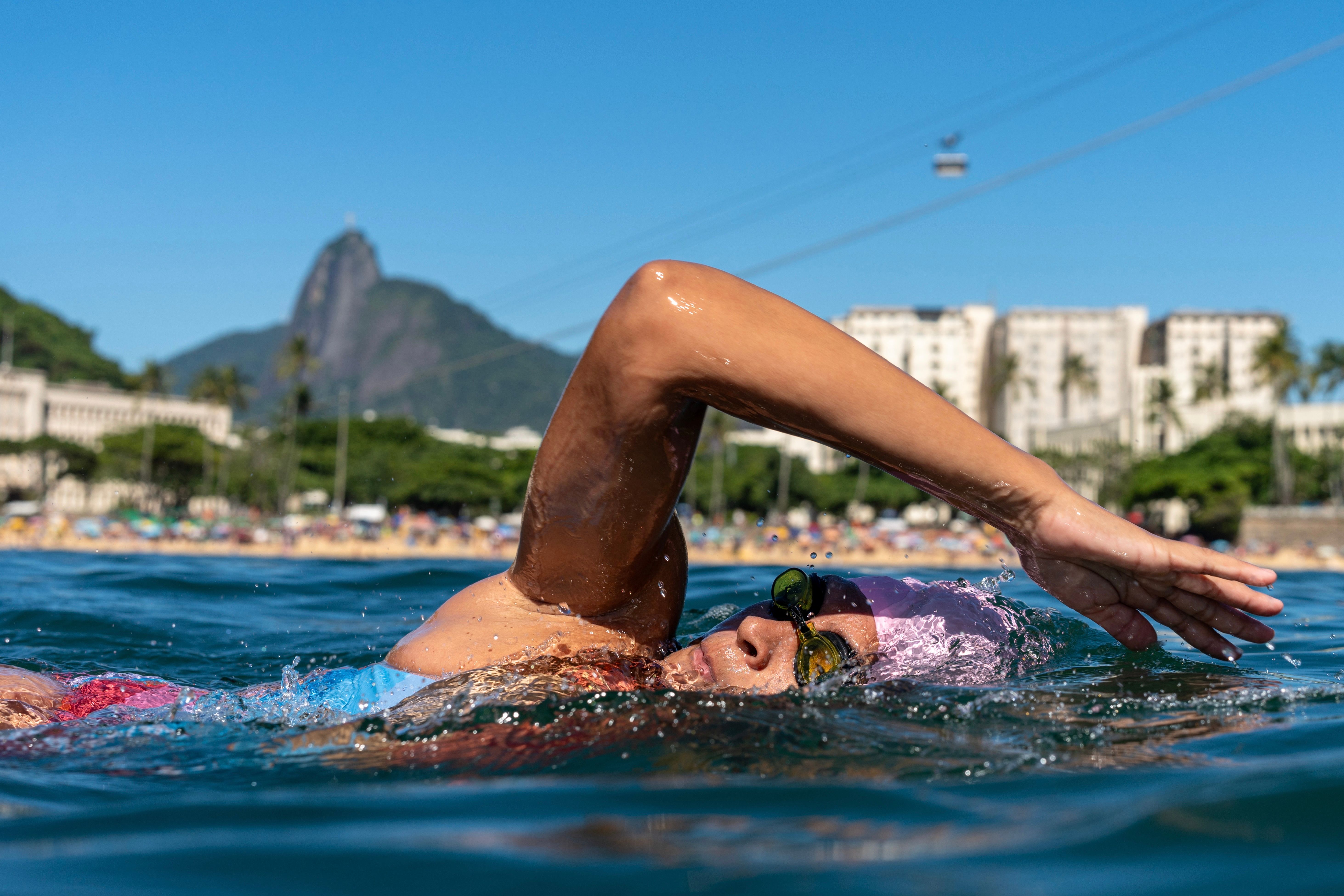 A woman swims in Rio's waters with Sugarloaf Mountain in the background on a sunny summer day.