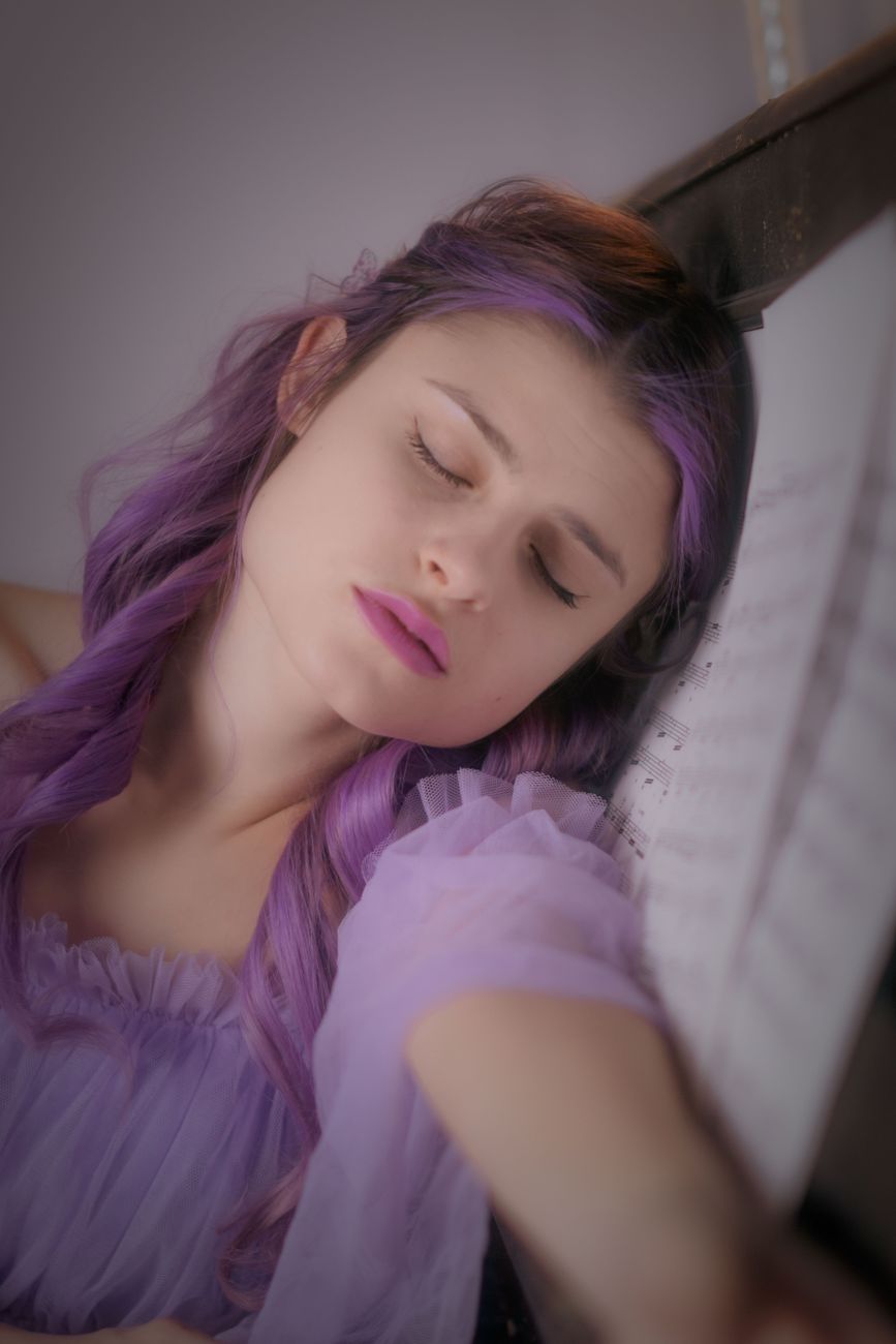 Elegant young woman with purple hair and tulle dress, relaxing indoors.