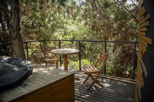 Peaceful outdoor balcony surrounded by trees with wooden chairs and table, perfect for relaxation.