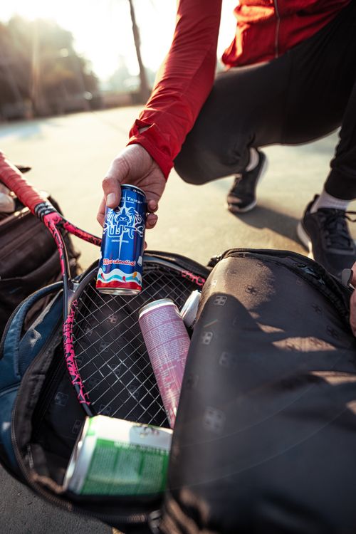 Free A person reaches for an energy drink from a tennis bag on a sunny day, emphasizing sport and refreshment. Stock Photo