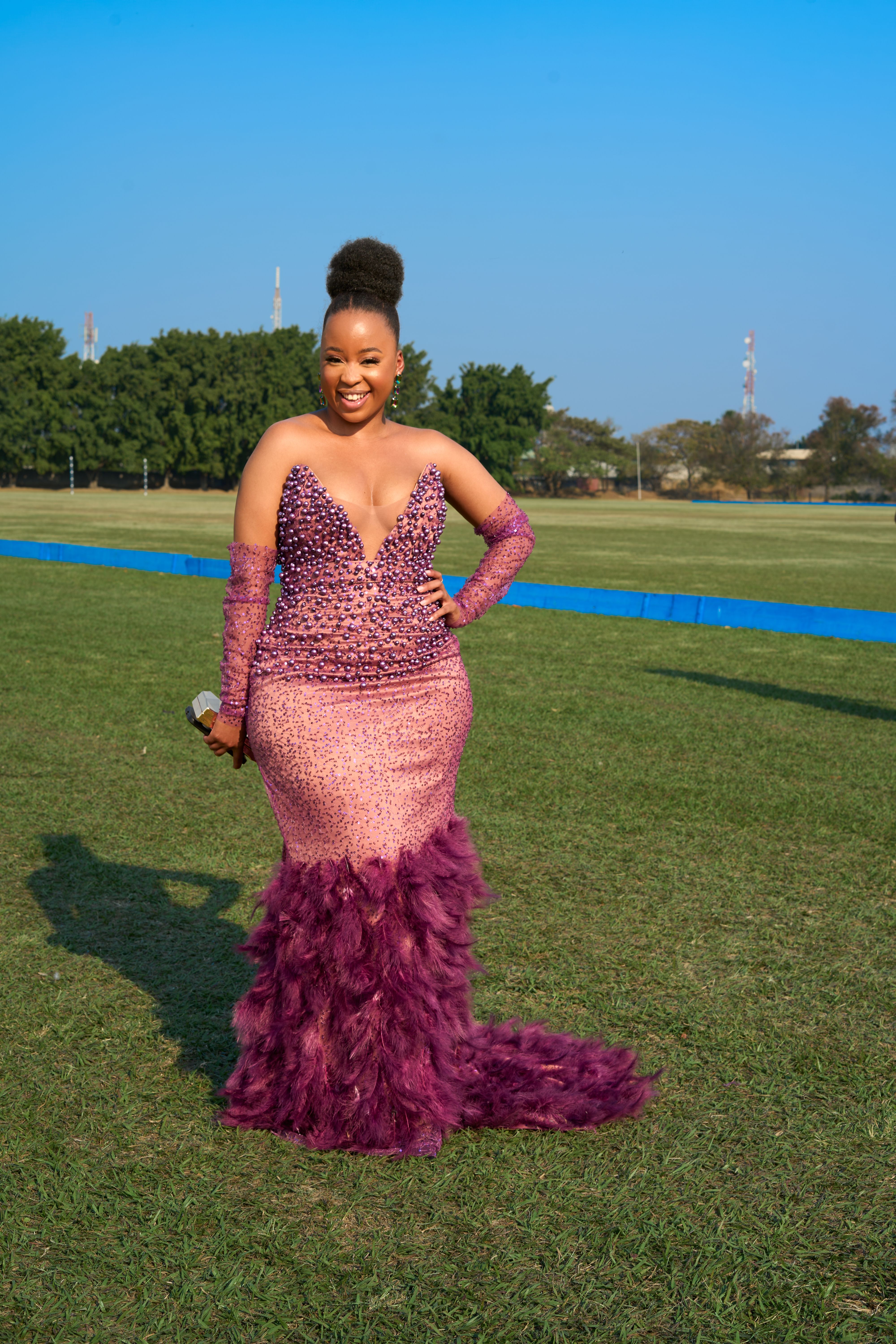 African woman in a pink, elegant dress posing on grass in sunlight.