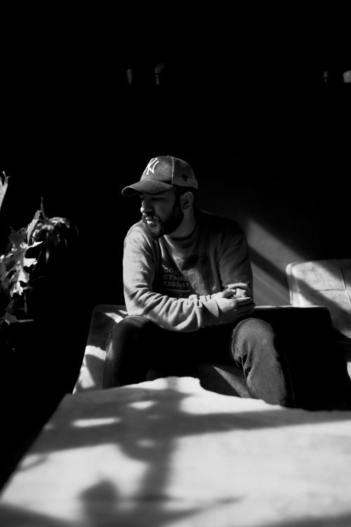Free Black and white portrait of a man in a cap and sweater sitting in a sunlit room. Stock Photo