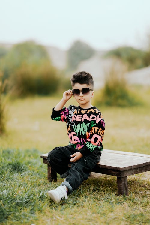 Boy Sitting on Wooden Bench on a Field 