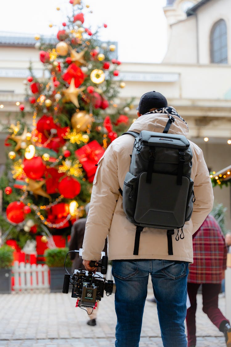 Back View Of A Man Holding A Professional Camera Standing In Front Of A Christmas Tree