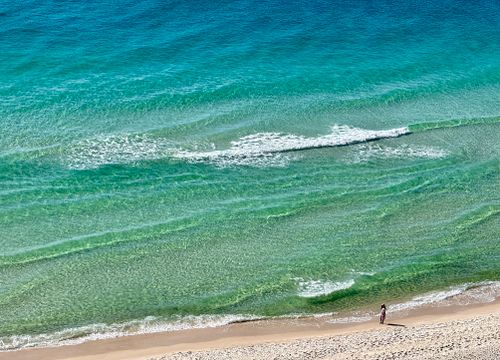 Free Peaceful aerial shot of a person walking along a tropical beach with turquoise waves. Stock Photo