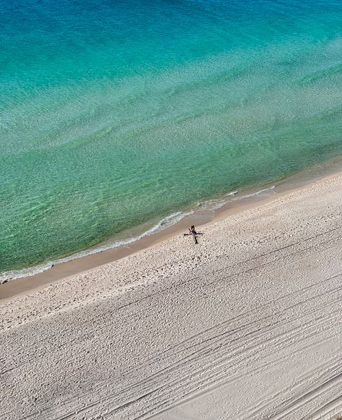Free A stunning aerial view of a tropical beach with turquoise water and a lone sunbather on the sandy shore. Stock Photo